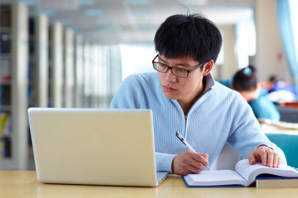 istock One male asian college student study in the library with laptop on table 667632868