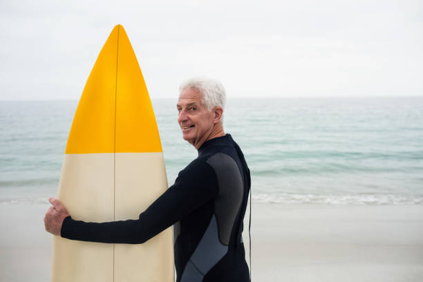 istock Happy senior man in wetsuit holding a surfboard 667649492