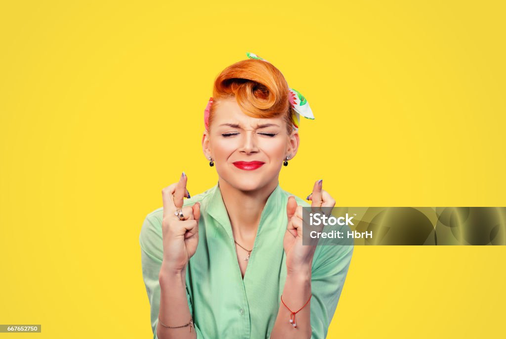 Closeup  hopeful beautiful young woman pin up style retro crossing her fingers eyes closed hoping asking best isolated yellow background. Human face expression emotions feeling attitude reaction Women Stock Photo