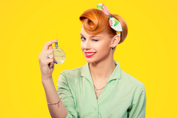Girl with perfume. Closeup red head beautiful young woman pretty smiling pinup girl green button shirt holding bottle of perfume and smelling aroma looking at you camera, retro vintage 50's hairstyle stock photo