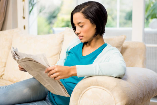 istock Attractive brunette reading newspaper on the sofa 667656884