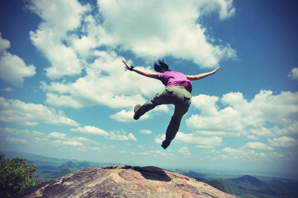 istock cheering successful young woman jumping on mountain peak 667672002