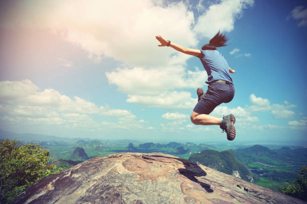 istock cheering successful young woman jumping on mountain peak 667675790