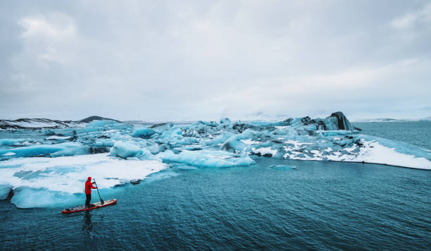 hermosa vista de icebergs glacier lagoon con un tipo paddle boarding (sup), calentamiento global y concepto de cambio climático - travel adventure winter cold fotografías e imágenes de stock