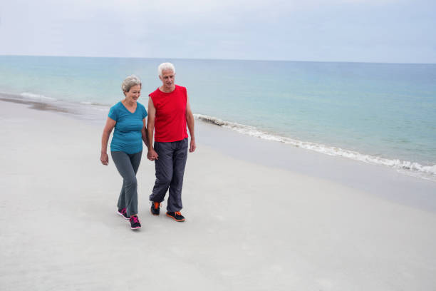 istock Senior couple holding hands and walking on the beach 667682574