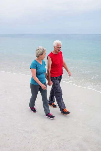 istock Senior couple holding hands and walking on the beach 667682684