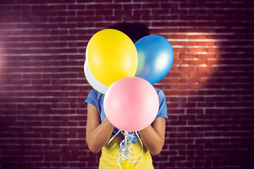 Young woman hiding behind balloons on a brick wall