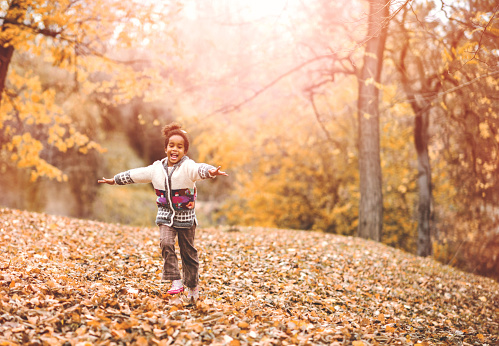 Happy African American girl enjoying in autumn day while running with her arms outstretched.