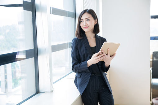 young woman wearing a black suit, using a tablet in her office