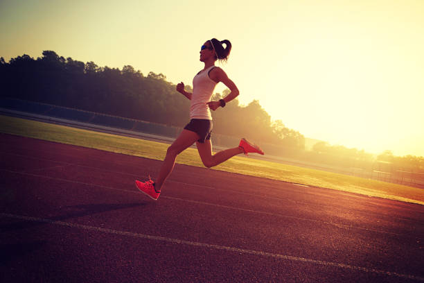 istock Young woman running during sunny morning on stadium track 667701782