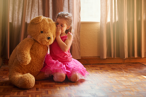 Shot of a little girl whispering something in her teddy bear's ear