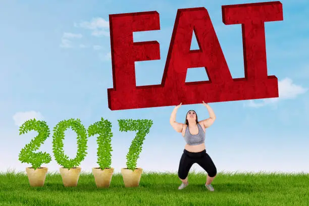 Overweight young woman standing on the grass while holding a fat word near number 2017