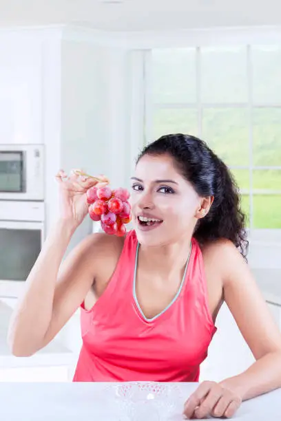 Young Indian woman looking at the camera with a bunch of fresh grapes at home