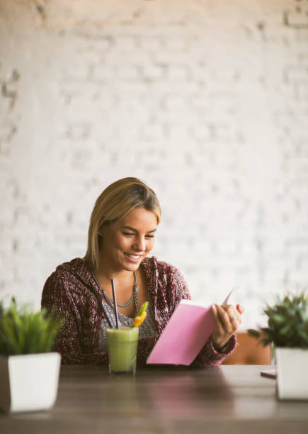 Happy woman enjoying while reading a book and having a healthy drink.
