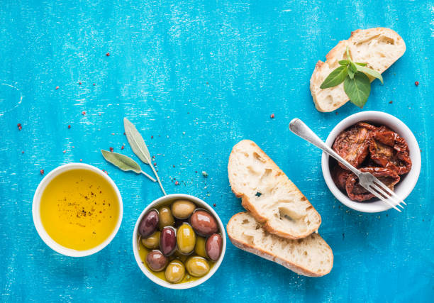 méditerranée collations ensemble. olives, huile, tomates séchées, herbes et pain ciabatta en tranches sur fond peint bleu - cuisine méditerranéenne photos et images de collection