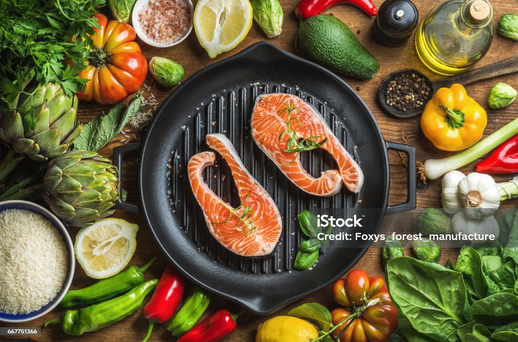 Abendessen kochen Ingredints. Rohen ungekochten Lachs Fisch mit Gemüse, Reis, Kräuter, Gewürze und Öl in Grillen Eisenpfanne über rustikale Holz Hintergrund - Lizenzfrei Mittelmeer Stock-Foto