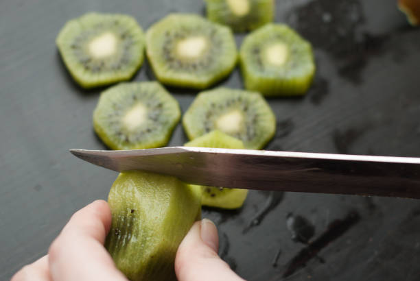 istock woman's hand cut KIWI into pieces on wooden Board, 667752494