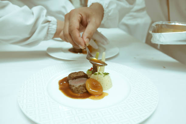 istock chef using chopsticks tong sliced beef put on the white plate in luxury dinner party, Blurry background with vintage color style. 667754636