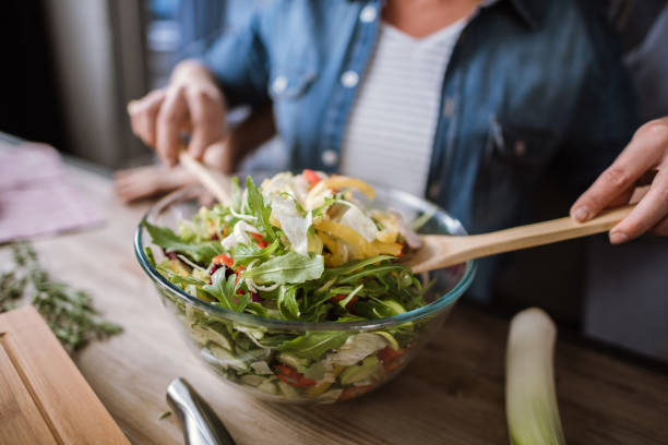 Close-up partial view of mature couple cooking vegetable salad in bowl