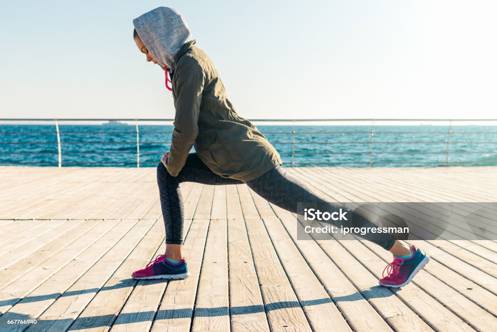 Woman in jacket and hood doing sports exercises on the beach in the morning Woman in jacket and hood doing sports exercises on the beach in the morning, wide angle Active Lifestyle Stock Photo