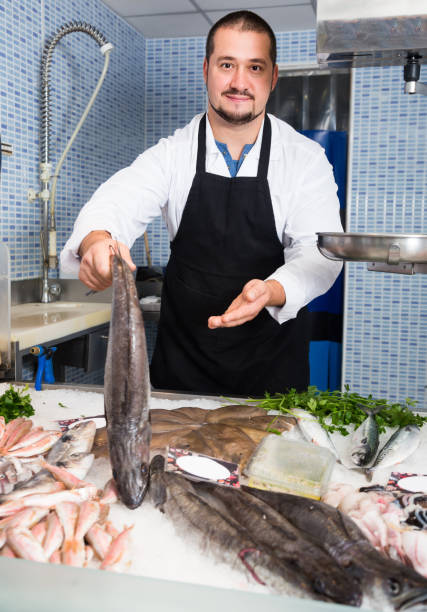 istock Laughing seller in black apron showing fish 667767336