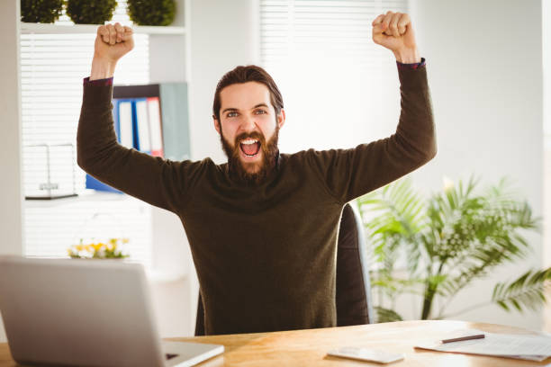 istock Hipster businessman cheering at his desk 667771282