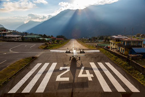 Airplane preparing for take off on Short Runway of small Airport ending at deep Canyon in Himalaya Nepal Mountains in Sunset Light