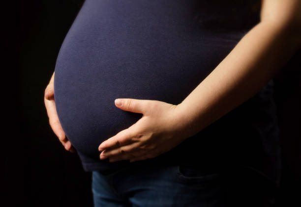 pregnant woman holding hands over belly on black background - teenage pregnancy fotos imagens e fotografias de stock