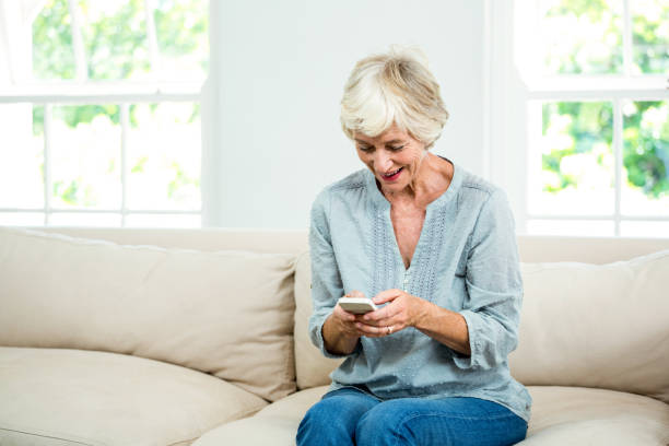 istock Smiling senior woman using mobile phone on sofa 667794864