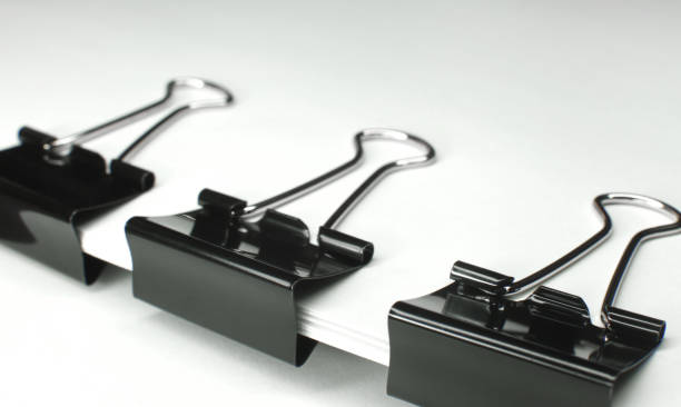 istock Black binder clips clamping the paper close up white background 667806414