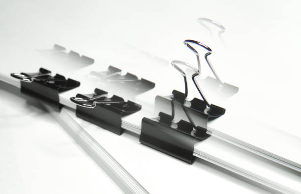 istock Black binder clips clamping the paper close up white background with lense distortion filter 667806440