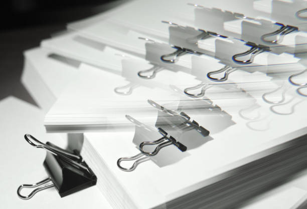 istock Black binder clips clamping the paper close up white background with lense distortion filter 667806494