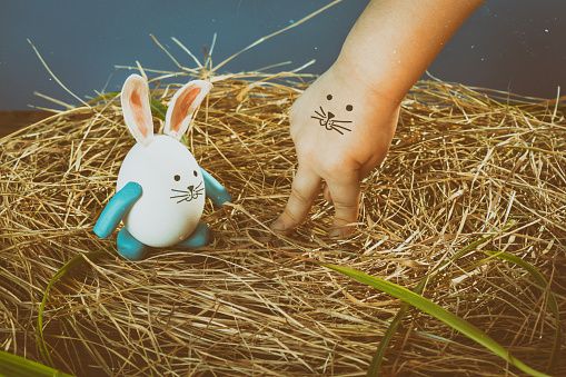 Funny easter rabbit and child hand with cute face. Nest from dry grass with green leaves. Face painted on a child's hand