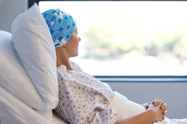 Cancer patient resting Young woman in bed suffering from cancer. Thoughtful woman battling with tumor looking out of window. Young patient with blue headscarf recovery in hospital on bed. brain tumour stock pictures, royalty-free photos & images