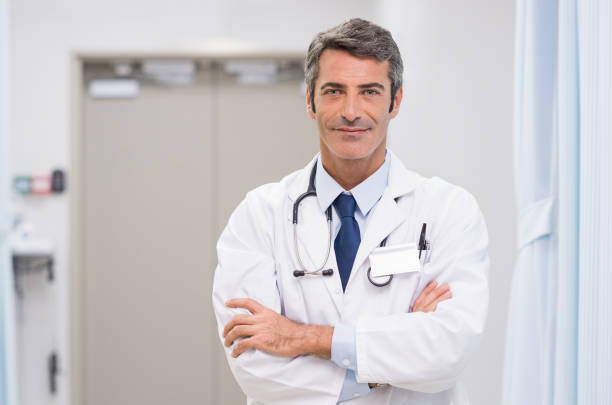 Mature doctor at hospital Portrait of smiling doctor with stethoscope around his neck at medical clinic. Happy smiling senior doctor at hospital lobby. Mature man feeling confident after a major operation and looking at camera."r smirking stock pictures, royalty-free photos & images