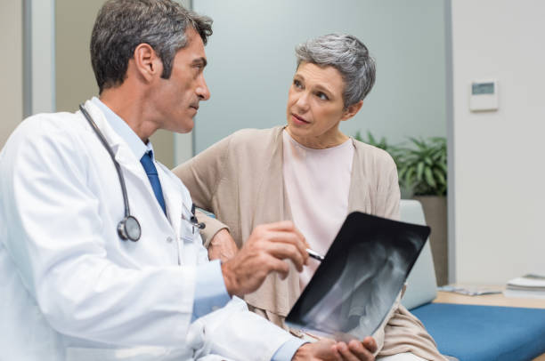 Doctor and senior patient Male doctor and senior patient discussing scan results at the office. Doctor showing to senior woman x-ray in a medical clinic. Mature doctor showing a radiography to his patient. osteoporosis stock pictures, royalty-free photos & images