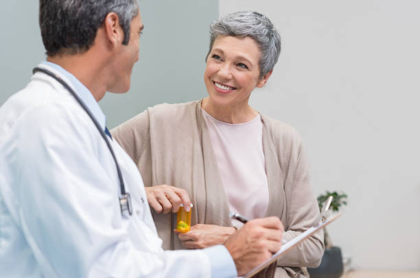 Patient and doctor talking Senior doctor in conversation with senior woman holding medicine box. General practitioner and patient discussing at office. Happy doctor discussing with patient and prescribes pills."r old woman smiling tablet stock pictures, royalty-free photos & images