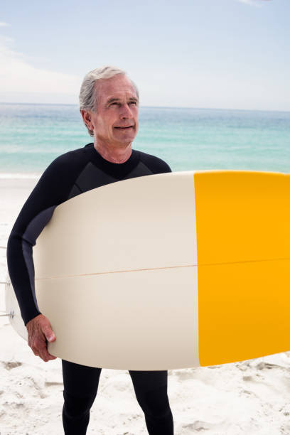 istock Happy senior man in wetsuit holding a surfboard 667825474