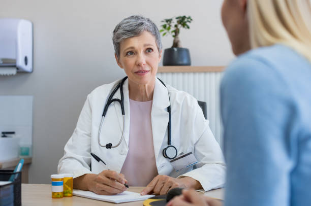 Doctor in a consultation Senior female doctor listening to patient explaining her painful in her office. Mature woman doctor consulting patient in hospital room. Doctor and patient discussing health issue in office. doctor general practitioner stock pictures, royalty-free photos & images