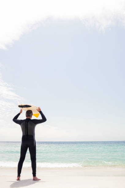istock Rear view of senior man holding a surfboard over his head 667831458