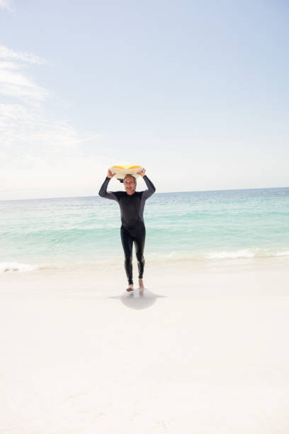 istock Senior man in wetsuit running with surfboard over his head 667831570