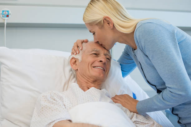 Daughter kissing senior father Young daughter kissing senior father on forehead in hospital bed. Cheerful old dad patient being kissed by daughter while recovering from disease in clinic. Lovely woman visiting old father at medical clinic. father daughter 80s stock pictures, royalty-free photos & images
