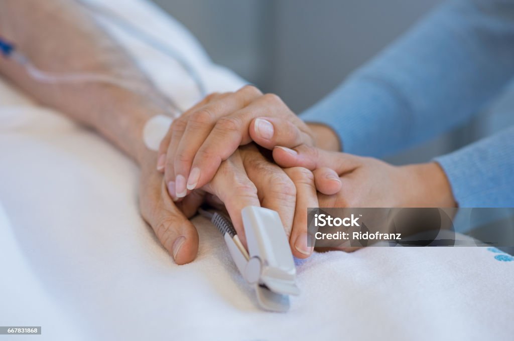 Take care of old patient Daughter holding the hand of an elderly father. Closeup of woman holding senior man hand in hospital. Close up of nurse holding old man hand with oxygen saturated probe on finger. Hospital Stock Photo