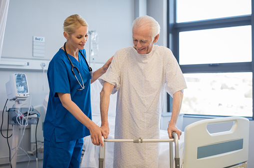 Nurse helping disabled man using walker in rehab center. Happy female nurse helping old patient to walk using walker in hospital. Doctor woman giving physical therapy to senior patient.