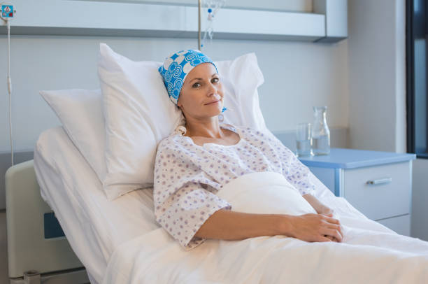 Cancer woman in hospital Young woman with tumor lying on hospital bed and looking at camera. Hopeful woman recovering from medical disease. Smiling woman with bandana on head resting in hospital ward after chemotherapy. metastasis photos stock pictures, royalty-free photos & images