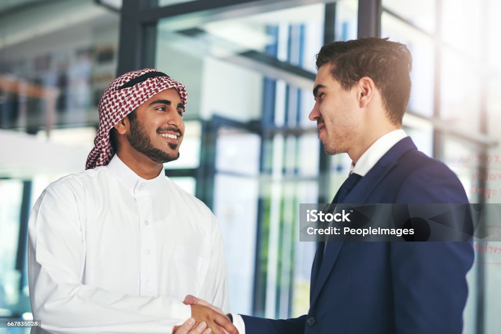 Business built on a mutual purpose Shot of a young muslim businessman shaking hands with an associate in a modern office Arabia Stock Photo