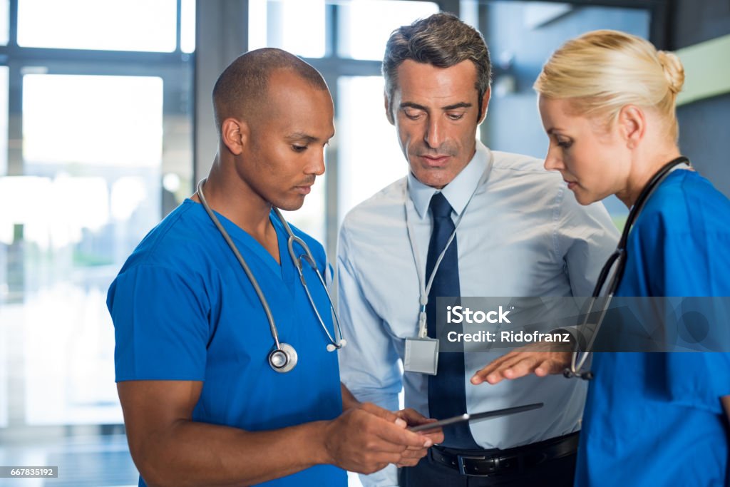 Medical conference Medical team interacting using digital tablet at modern hospital. Mature doctor and african surgeon working on digital tablet with nurse. Head physician working with his medical team at clinic. Healthcare And Medicine Stock Photo