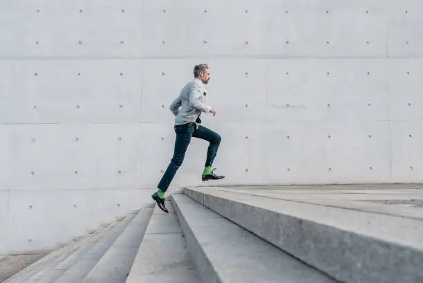 Photo of elegant bearded businessman running up stairs outdoors