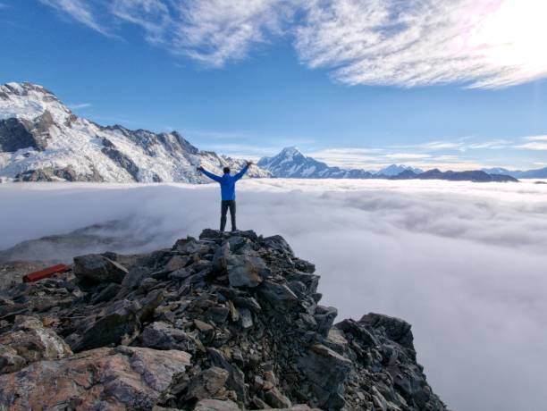 istock Man standing on mountain cliff over clouds looking to impressive mountain peak 667870034
