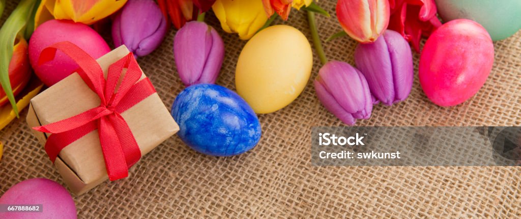 Spring tulips with colorful easter eggs and gift box Easter background with eggs and tulips. Holiday card with copy space, on brown cloth background. Backgrounds Stock Photo